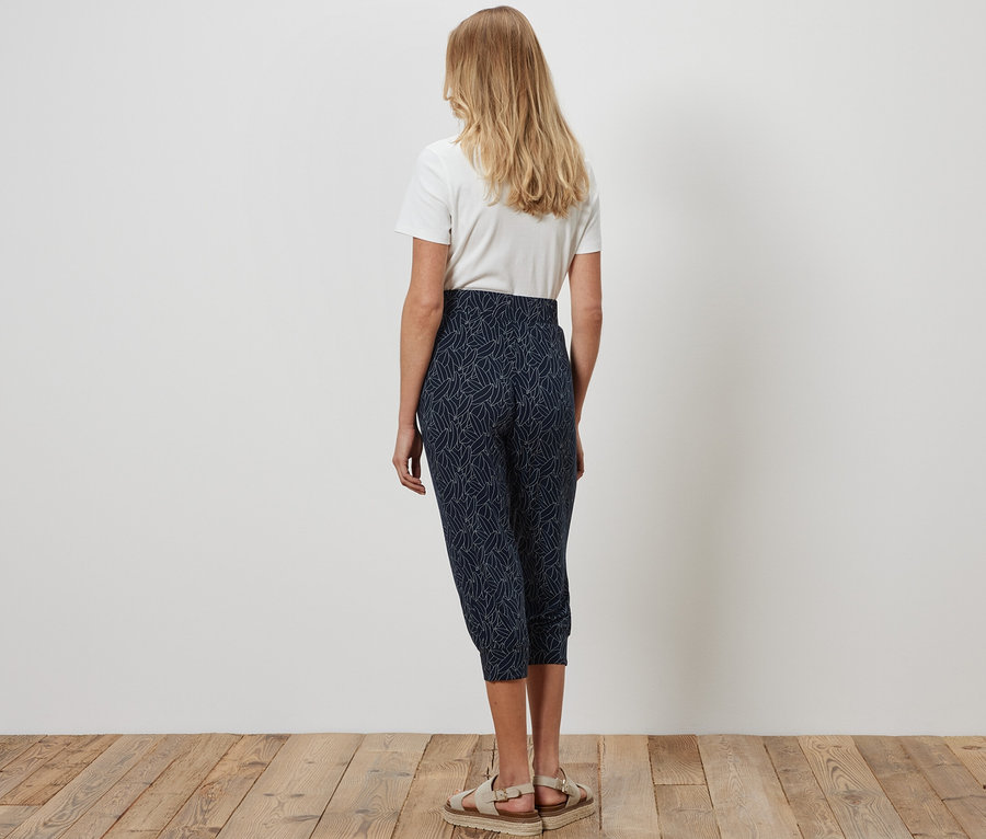 Eine Frau steht von hinten auf einem Holzboden und trägt eine blau-cremeweiße 3/4-Jerseyhose und ein weißes T-Shirt.