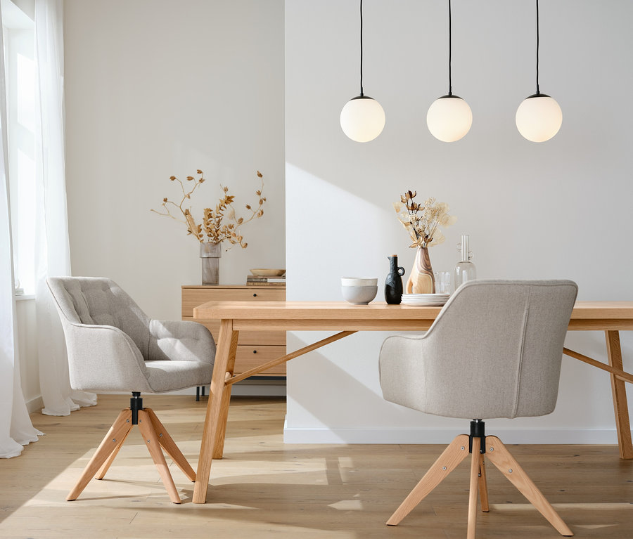 Zwei drehbare Dining-Stühle stehen an einem Holztisch. Über dem Tisch hängt eine Hängeleuchte mit Glaskugeln.