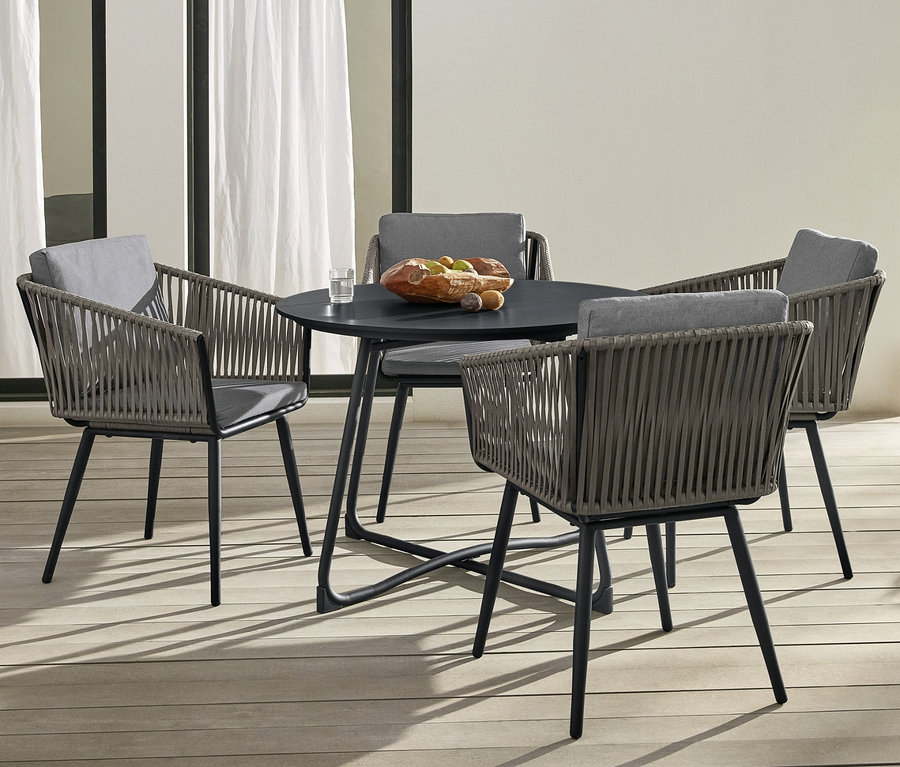 Vier Dining-Sessel »Jara« mit Textilgeflecht umgeben einen runden Gartentisch »Jara« mit Duraboard. Eine Frau sitzt auf einem Daybed »Jara« mit Textilgeflecht.