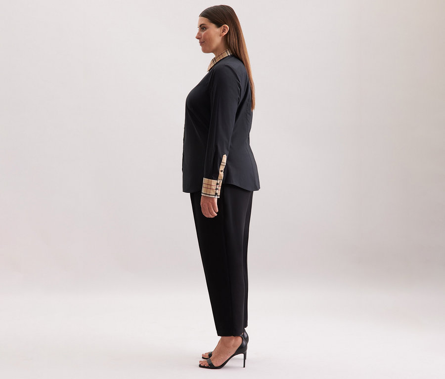 Frau trägt eine schwarze Seidensticker Popeline-Bluse mit Karodetail, schwarze Hose und schwarze Absätze.