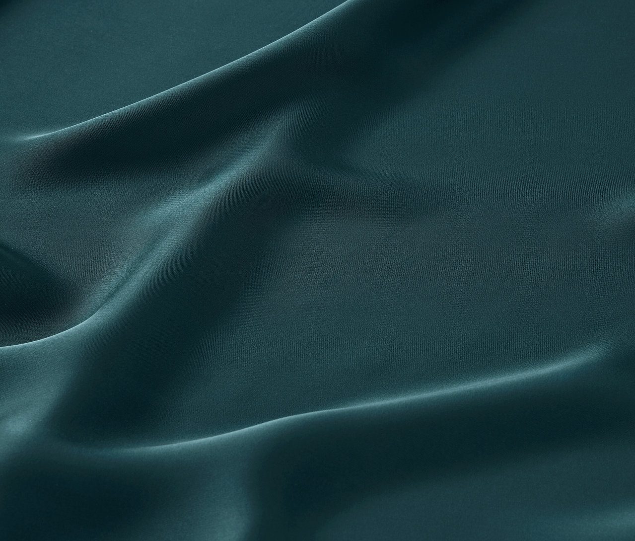 Nahaufnahme eines smaragdgrünen Satinstoffs mit sanften Falten.