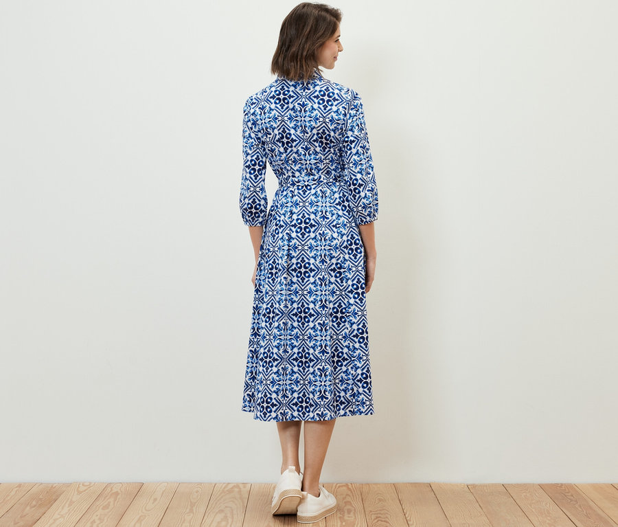 Frau steht mit dem Rücken zur Kamera und trägt ein bedrucktes Midikleid.