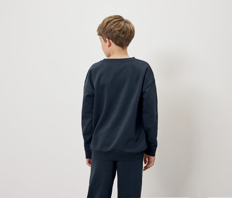 Junge in dunkelblauem Sweatshirt und Hose, der mit dem Rücken zur Kamera steht.