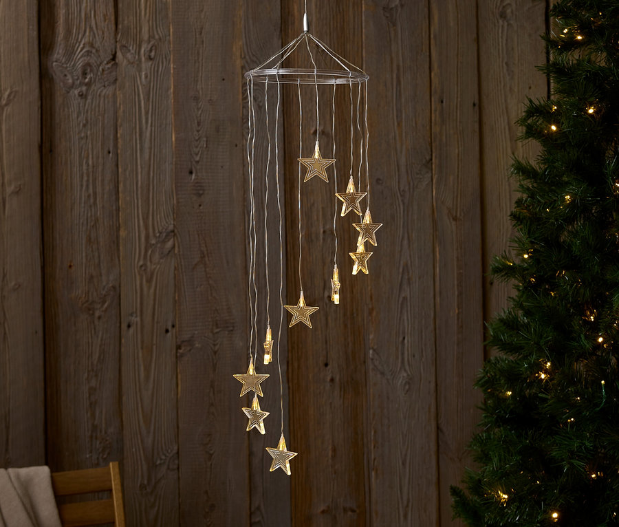 Eine hängende Dekoration mit Sternenlichtern vor einer Holzwand und einem Weihnachtsbaum.