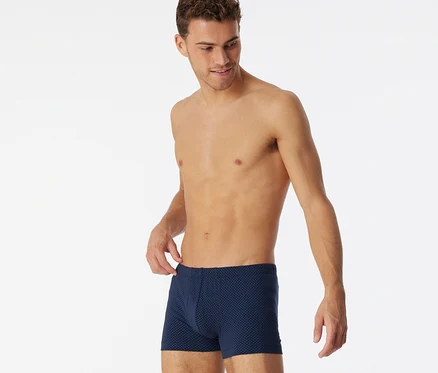 Mann trägt dunkelblaue SCHIESSER Shorts mit Alloverprint und fasst an den Bund.