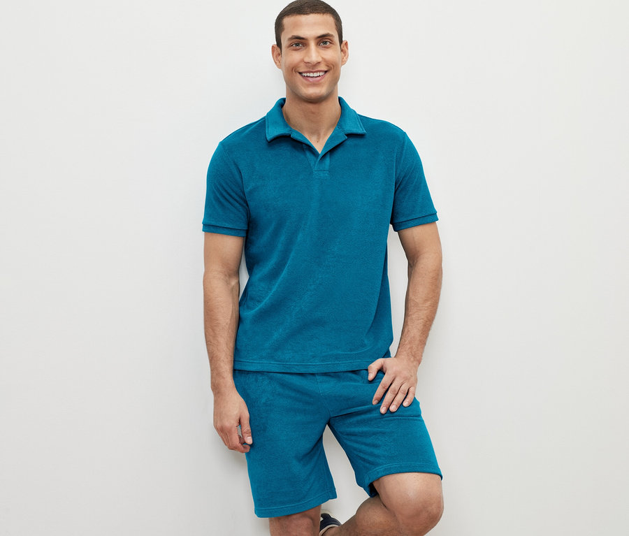 Mann posiert in einem petrolfarbenen Frottee-Poloshirt und Shorts.
