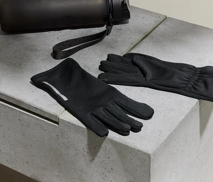 Schwarze Handschuhe und eine Wasserflasche liegen auf einer Betonoberfläche.
