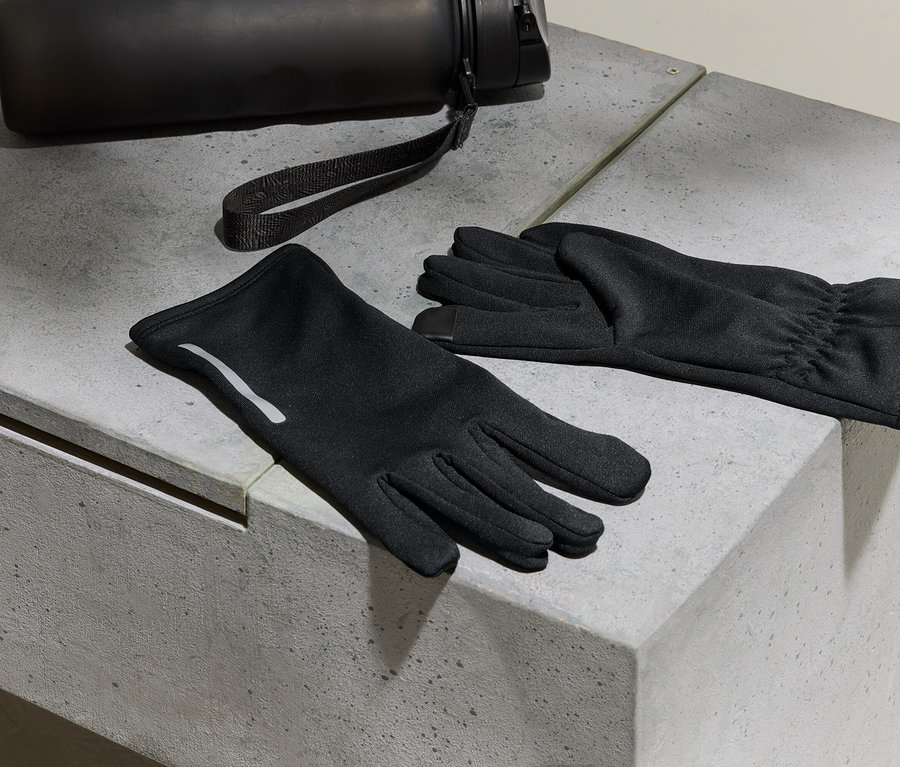 Schwarze Handschuhe und eine Wasserflasche liegen auf einer Betonoberfläche.