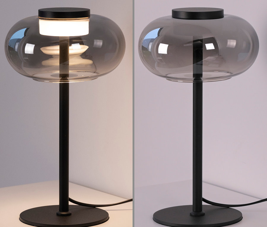 Zwei graue Tischlampen mit schwarzen Sockeln auf einem weißen Tisch, eine Lampe leuchtet.