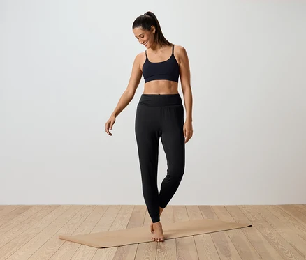 Frau steht auf einer Yogamatte und trägt einen schwarzen Sport-BH und schwarze Leggings.