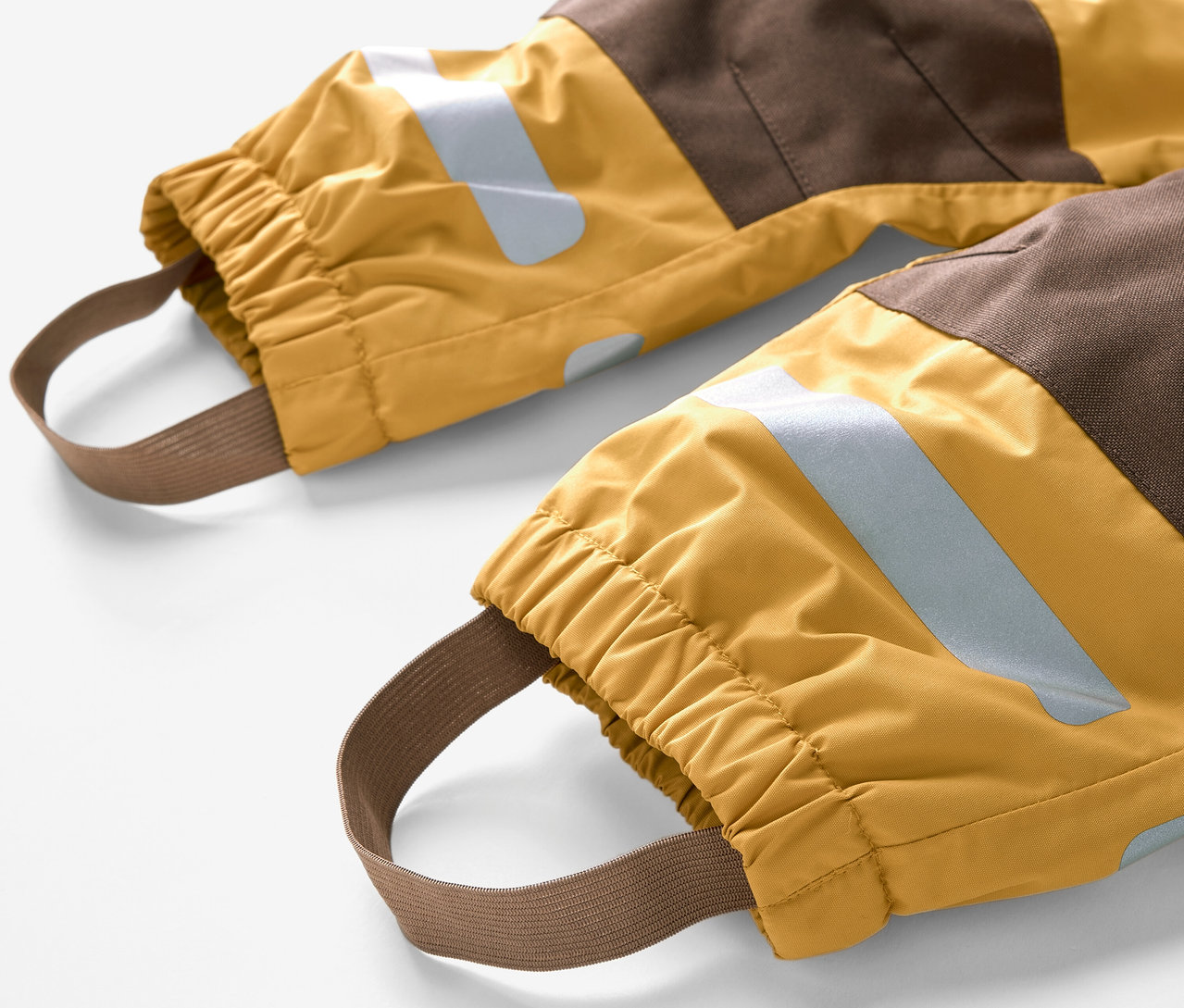 Detailansicht eines Kinder-Regen-Einteilers mit braunen und gelben Farbblöcken und elastischen Fußschlaufen.