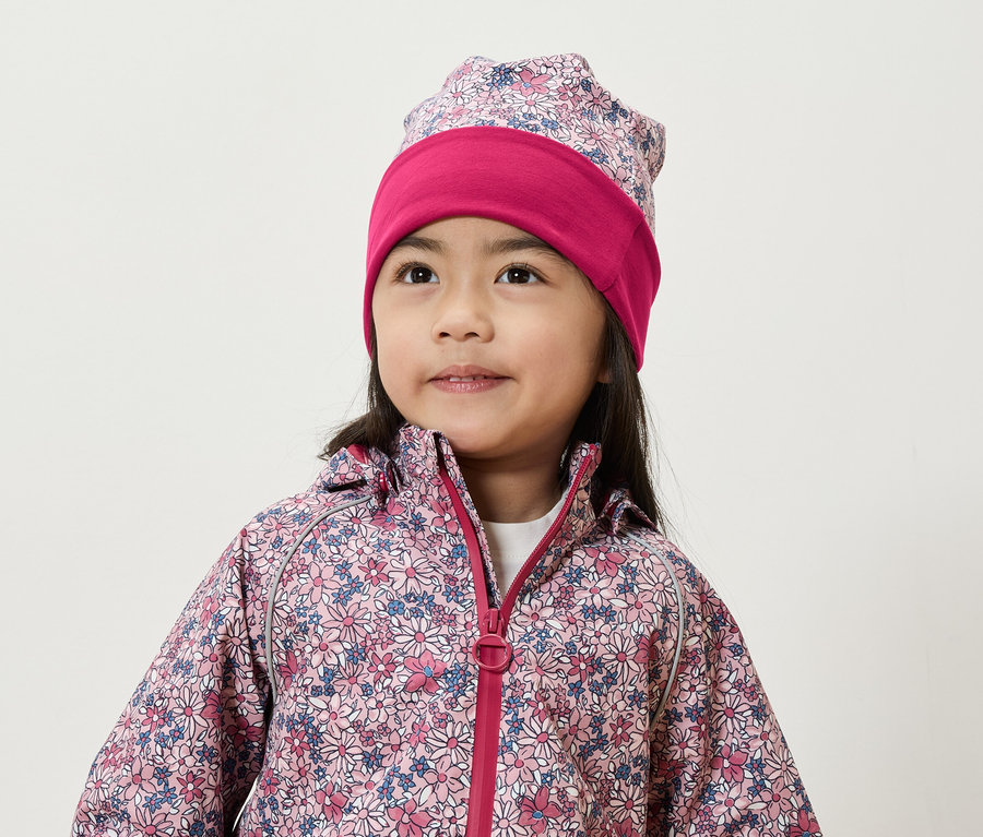 Lächelndes Mädchen trägt eine Blumenjacke und Mütze.
