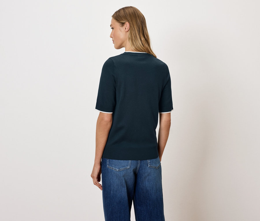 Frau posiert in einem dunkelblauen Oberteil und Jeans mit dem Rücken zur Kamera.