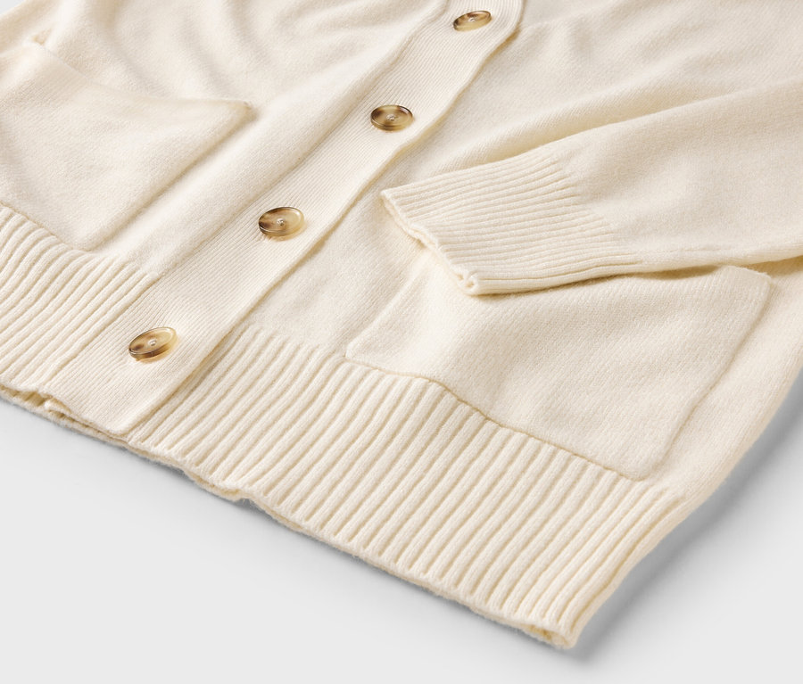 Detailaufnahme einer cremefarbenen Strickjacke mit Knöpfen und Taschen.