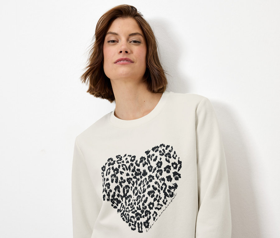 Frau trägt ein cremefarbenes Sweatshirt mit einem Leopardenmuster-Herz.