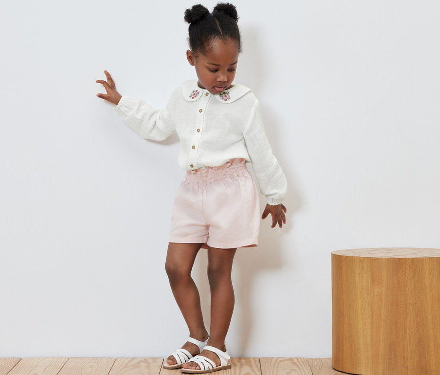 Mädchen tanzt in Kinder-Musselin-Bluse, rosa Shorts und Sandalen.