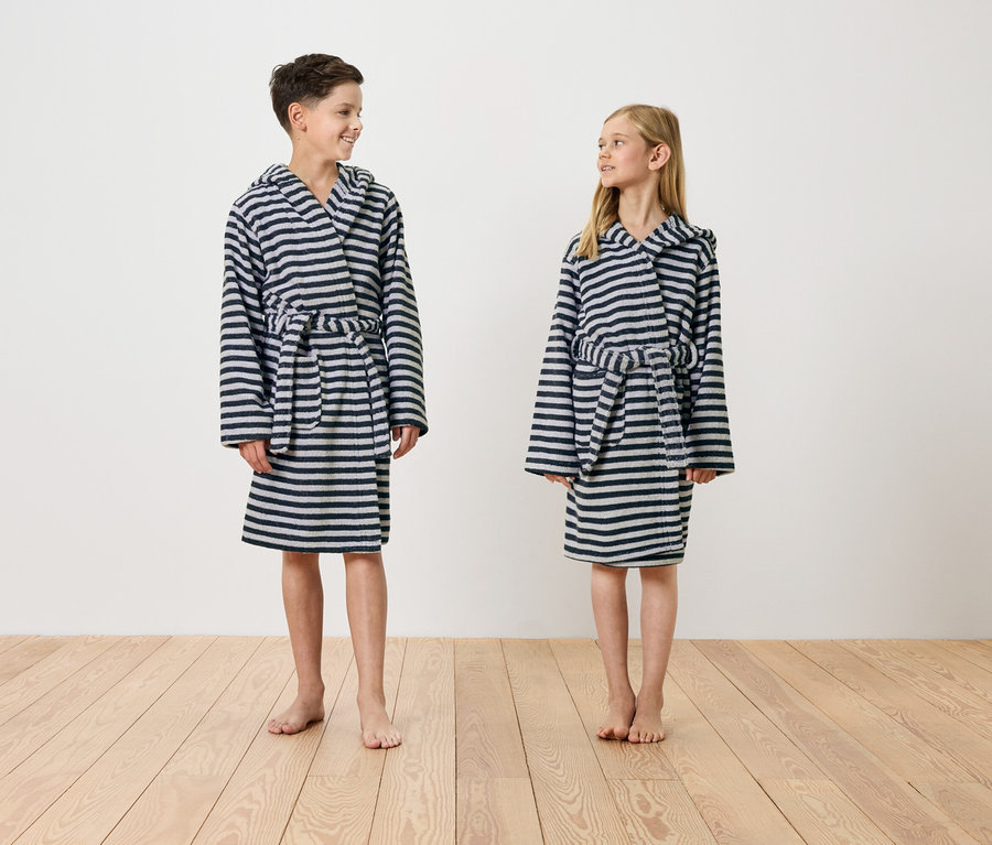 Ein Junge und ein Mädchen stehen barfuß auf einem Holzboden und tragen gestreifte Bademäntel mit Kapuze.
