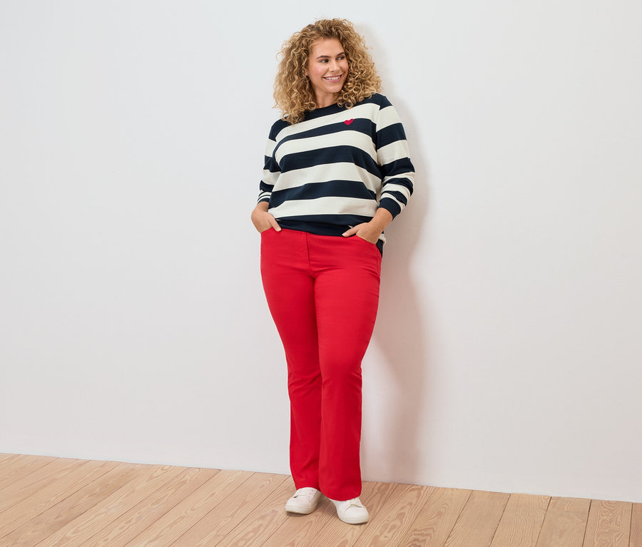 Frau mit lockigem Haar trägt ein gestreiftes Oberteil und eine rote Hose.