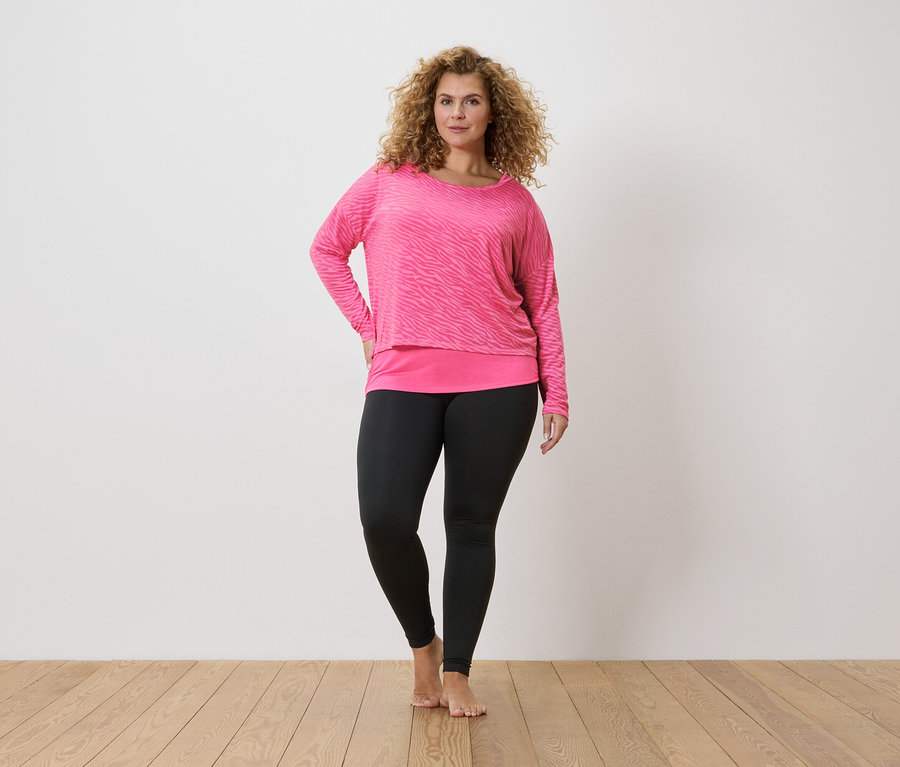 Frau mit lockigem Haar, die ein pinkes Zebra-Langarmshirt und schwarze Leggings trägt.