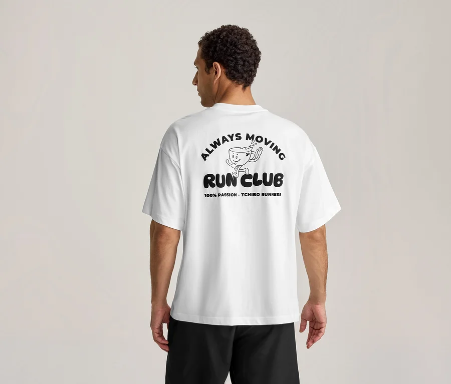 Mann von hinten in einem weißen Sportshirt mit schwarzem Aufdruck "ALWAYS MOVING RUN CLUB" und laufender Kaffeetasse.
