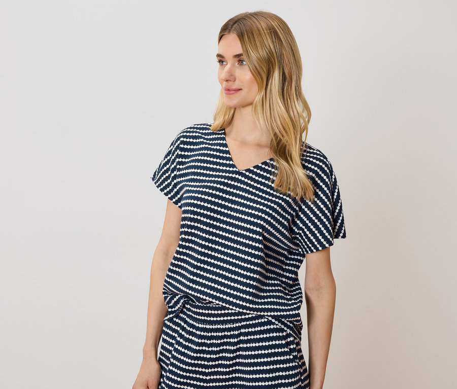 Frau mit blonden Haaren trägt ein blau-weiß gestreiftes T-Shirt und einen Rock.