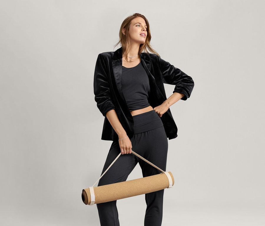 Frau trägt ein schwarzes Da. 2-in-1-Sportshirt und hält eine Yogamatte.