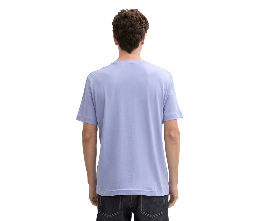 Rückansicht einer Person mit lockigem Haar, die ein hellblaues T-Shirt und dunkle Jeans trägt.