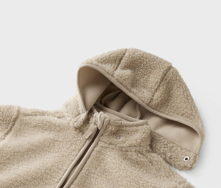 Nahaufnahme einer beigen Teddy-Fleece-Jacke mit Kapuze und Reißverschluss.