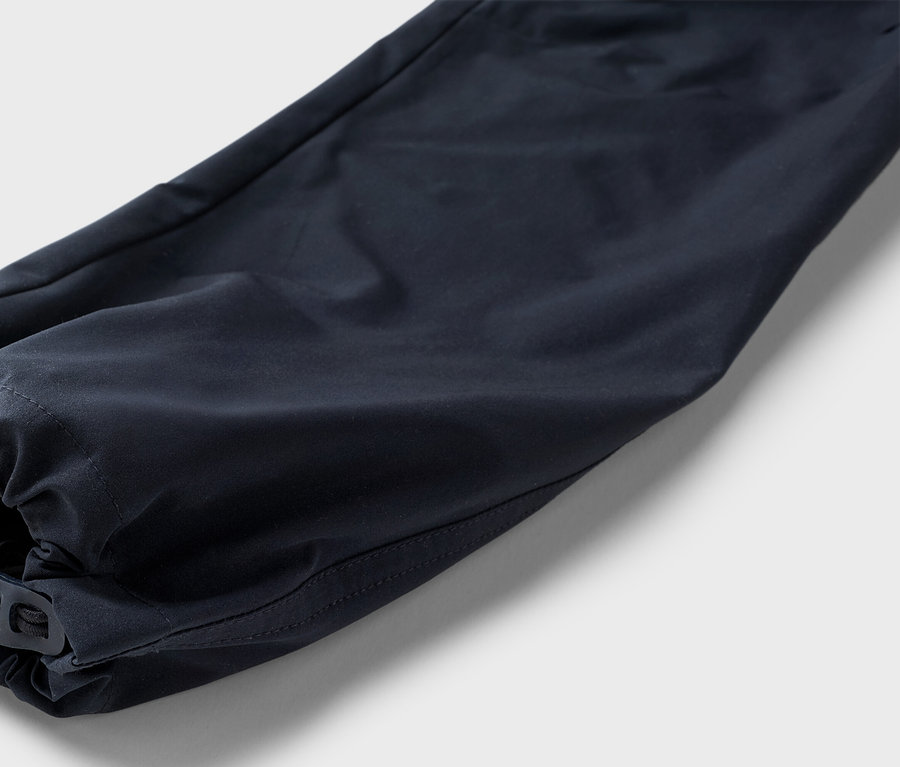 Nahaufnahme eines marineblauen Hosenbeins mit elastischem Saum und verstellbarem Knebelverschluss vor einem neutralen Hintergrund.