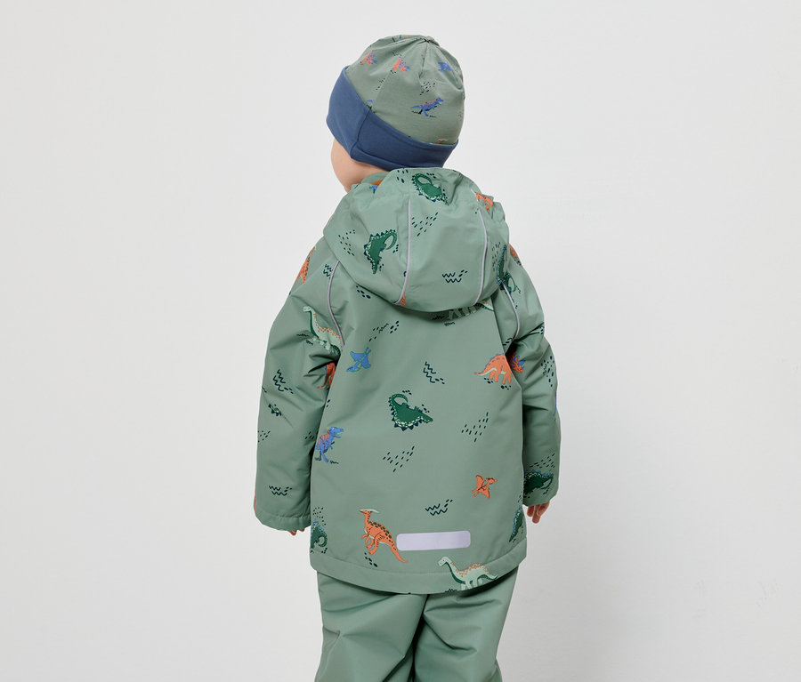 Rückansicht eines Kindes mit Mütze und grünem Dino-Overall vor einem weißen Hintergrund.