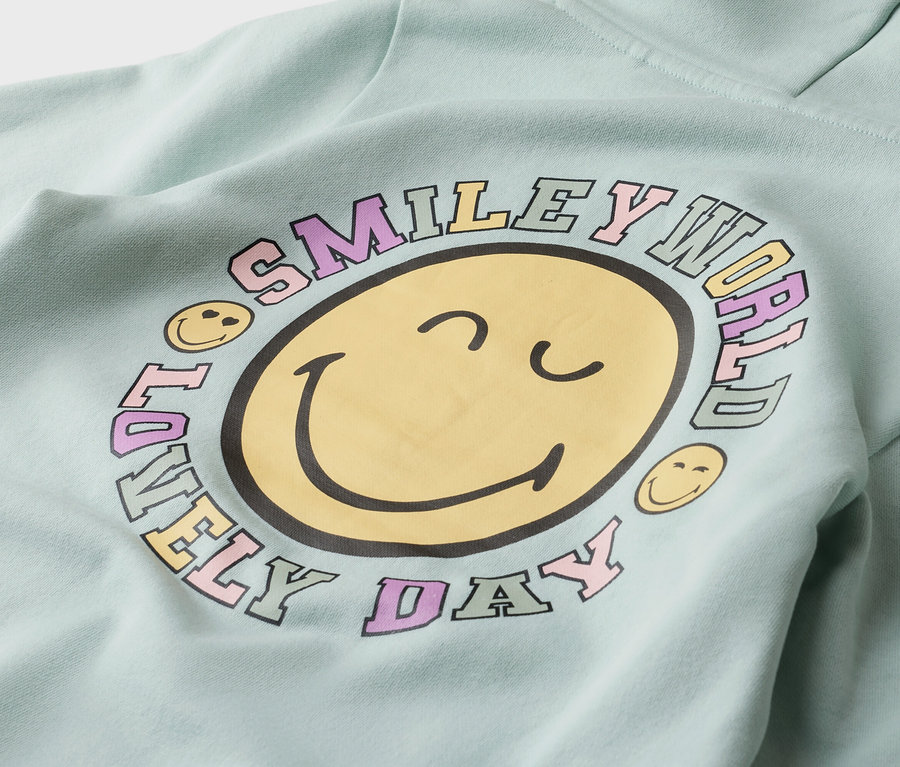 Nahaufnahme eines mintgrünen Hoodies mit einem gelben Smiley-Aufdruck, umgeben von der Aufschrift "Smiley World Lovely Day".