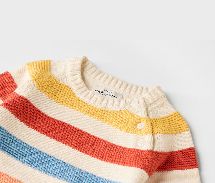 Nahaufnahme einer gestreiften Kinderstrickjacke in den Farben Rot, Gelb und Blau mit weißen Knöpfen.