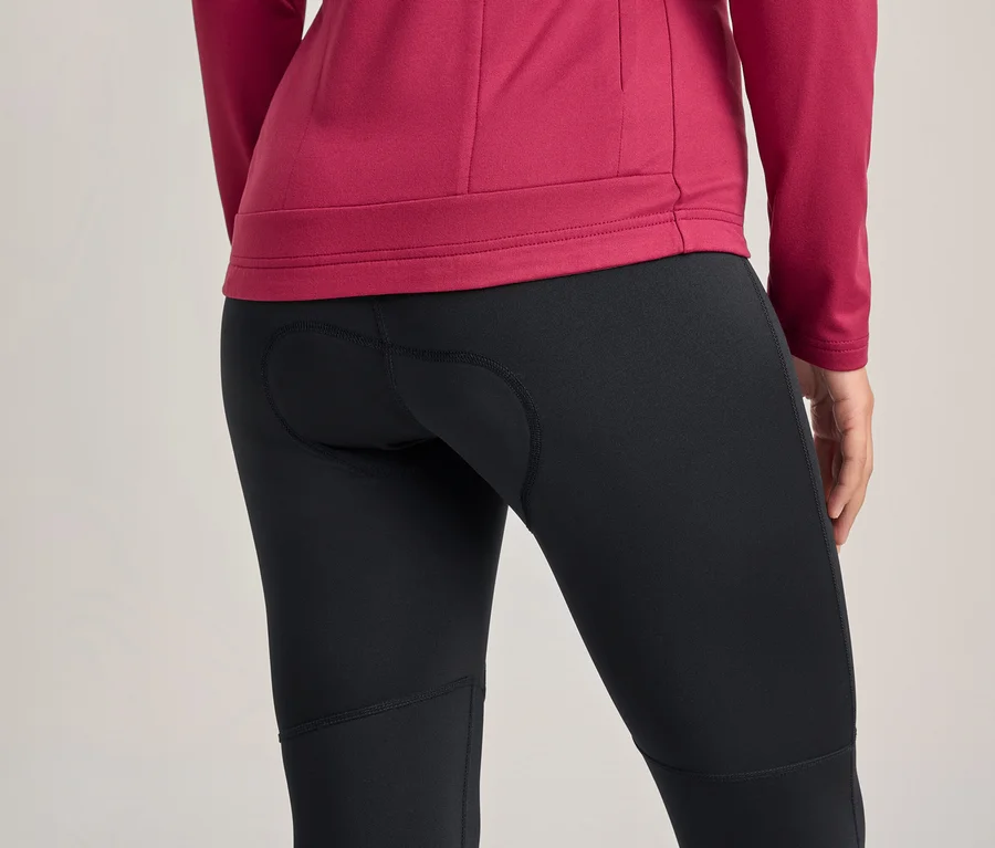 Person von hinten in einem magentafarbenen Langarmshirt und schwarzen Radhosen mit sichtbarem Sitzpolster.