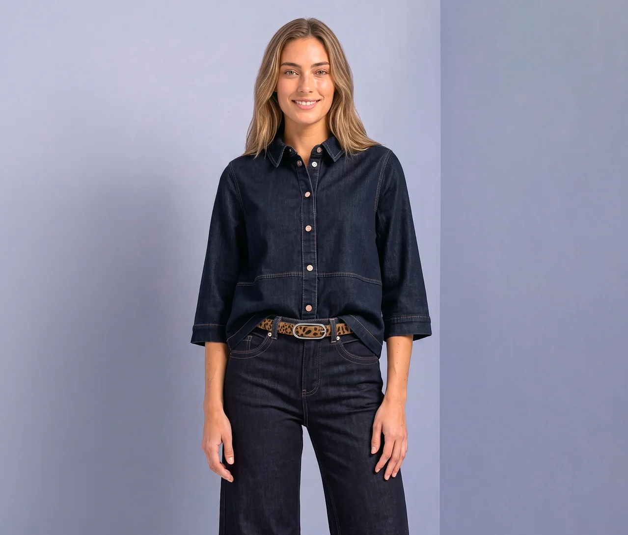 Eine lächelnde Frau mit langen blonden Haaren trägt eine dunkelblaue Street One Hemdbluse aus Denim mit Dreiviertelärmeln und hellen Knöpfen, dazu eine dunkelblaue Jeans und einen Leopardenmuster-Gürtel mit ovaler Schnalle.