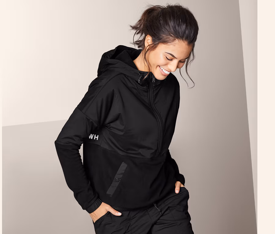 Frau trägt einen schwarzen Hybrid-Fleecesweater und eine schwarze Hose.