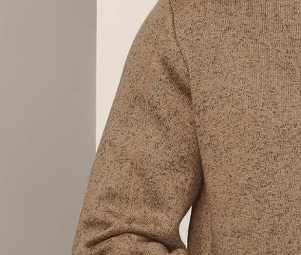 Mann posiert in Strickfleece-Midlayer und dunkelblauen Jeans.