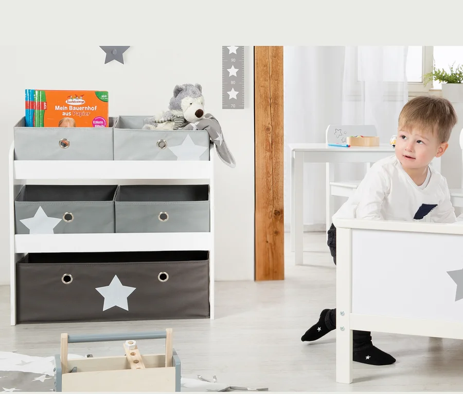 Junge lehnt an weißem Bett mit grauem Stern. Im Hintergrund roba Spielregal "Stars" mit Spielzeug.