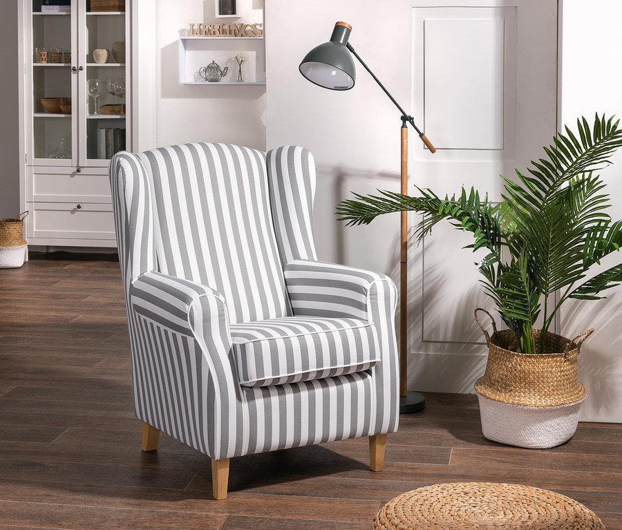 Ein »Luke« Ohrensessel mit grauen und weißen Streifen steht im Raum, daneben eine Lampe und eine Pflanze in einem Korb.