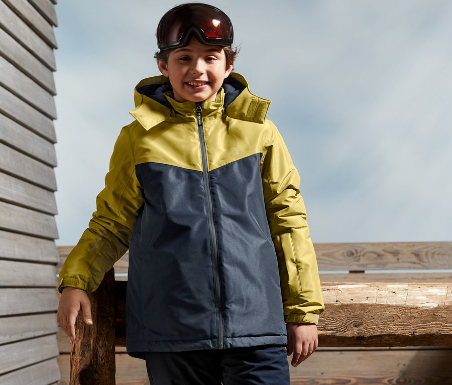 Ein Junge steht draußen und trägt eine Jungen-Skijacke.