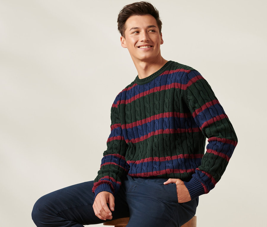 Mann sitzt auf einem Hocker und trägt einen Strickpullover.