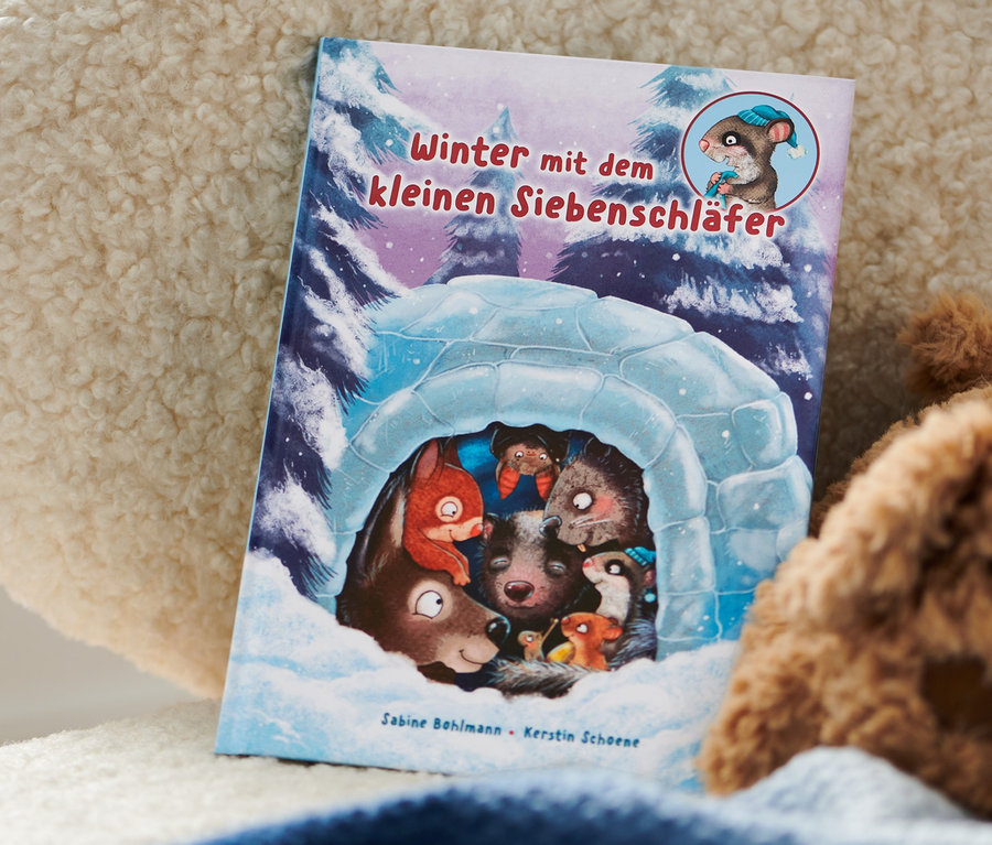Buch »Winter mit dem kleinen Siebenschläfer« liegt auf einem flauschigen Sessel neben einem Teddybär.