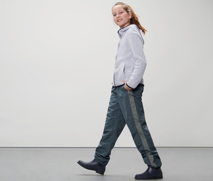Mädchen geht in Kinder-Regenhose und Gummistiefeln.