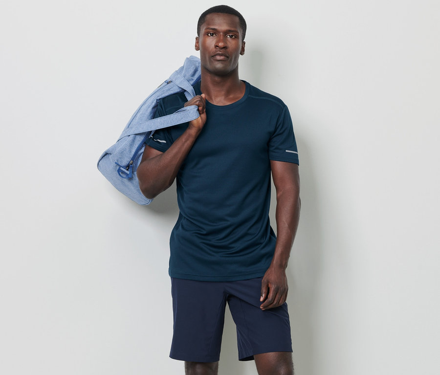 Mann posiert mit einer blauen Tasche über der Schulter und trägt ein dunkelblau meliertes Funktionsshirt.
