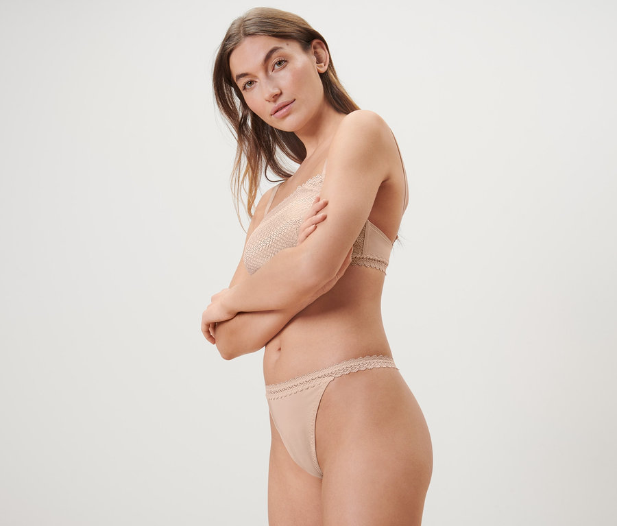 Frau posiert in beigem Spitzen-BH und 5 Strings.