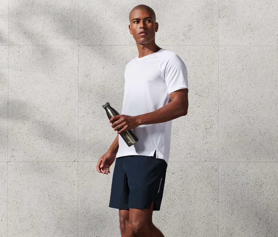 Mann im weißen T-Shirt hält eine Wasserflasche und trägt marineblaue Sportshorts.