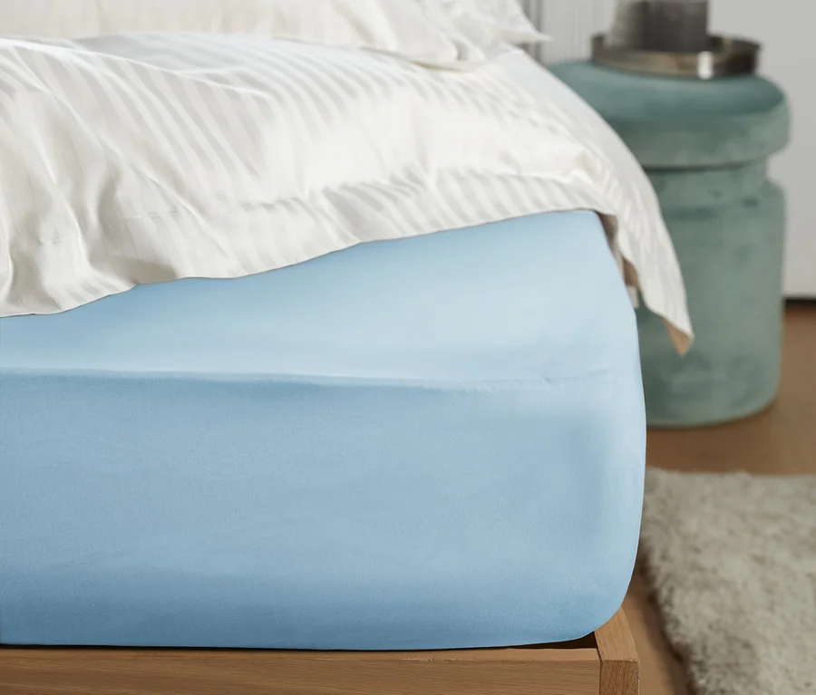 Blaues Perkal-Spannbettlaken in Normalgröße auf einem Bett.