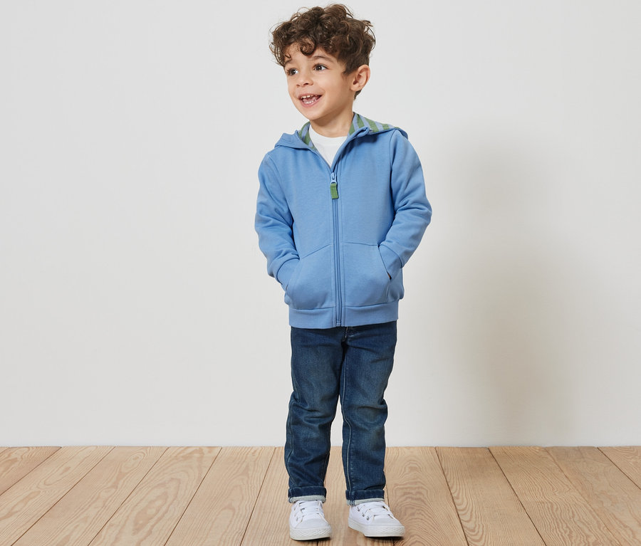 Junge trägt eine Kinder-Sweatjacke mit angerauter Innenseite, Jeans und Turnschuhe.