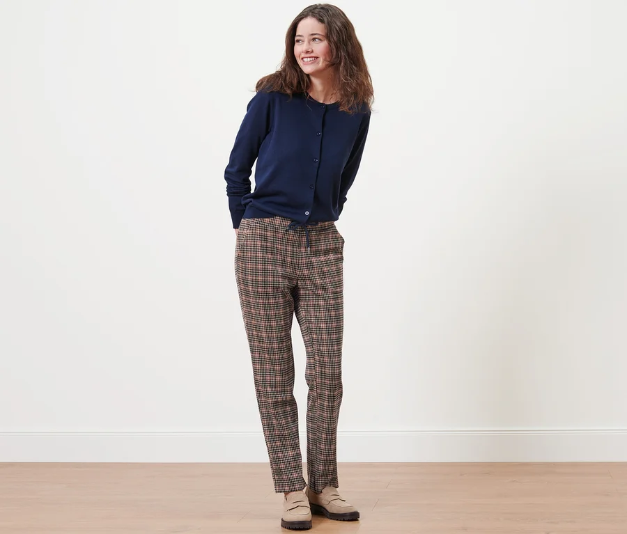 Eine Frau steht und trägt eine marineblaue Strickjacke und eine Joggpants mit Hahnentritt-Dessin.