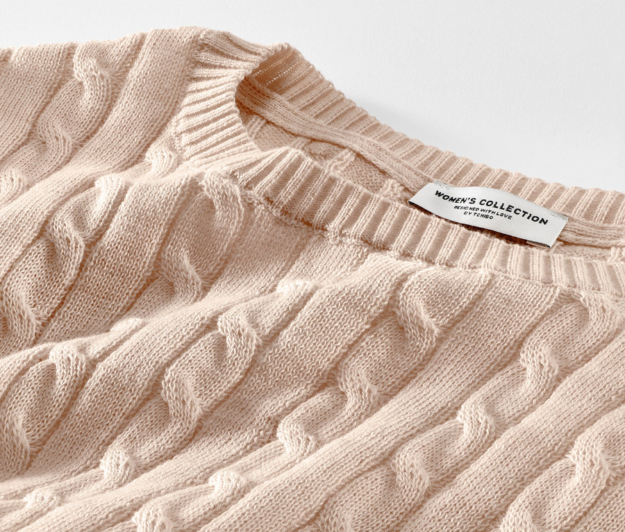 Detailaufnahme eines cremefarbenen Zopfstrickpullovers.