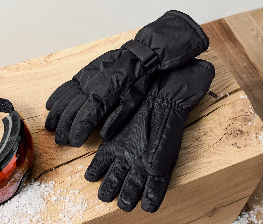 Zwei Skihandschuhe liegen auf einem Holzblock neben einer Skibrille.